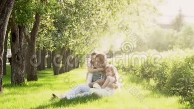 妈妈和两个女儿<strong>坐在</strong>苹果树附近的草地上。 日落时<strong>公园里</strong>的孩子和母亲。 投标书